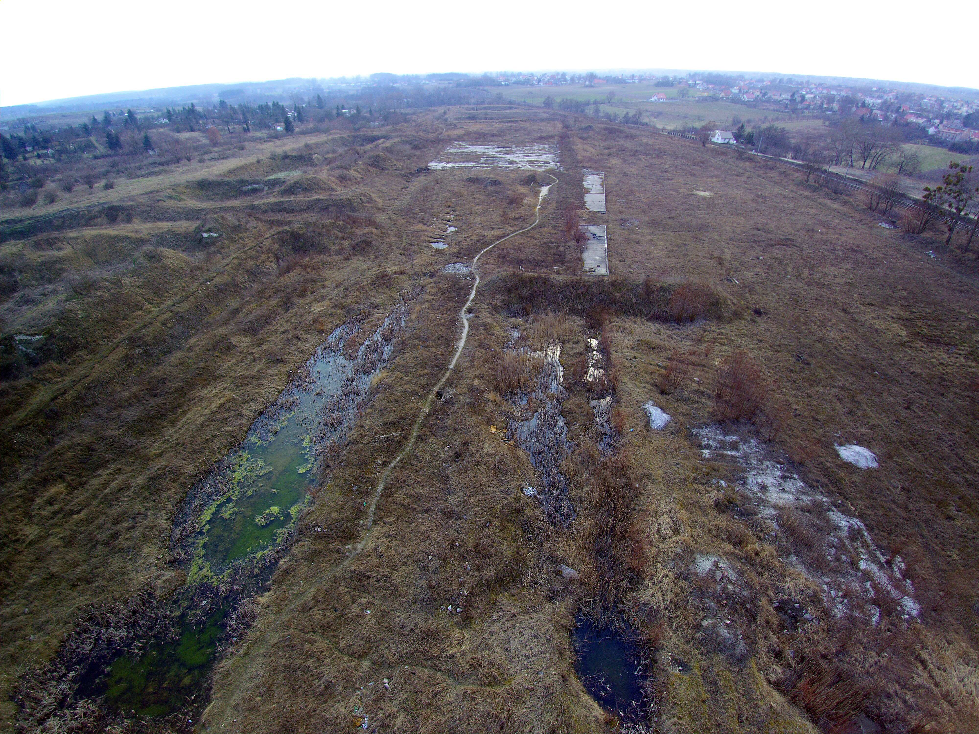 Zdjęcie przedstawia jeden z pustych terenów pofabrycznych w miejscowości Pelpin. Na zdjęciu widać łąki, pola, brak zabudowań.