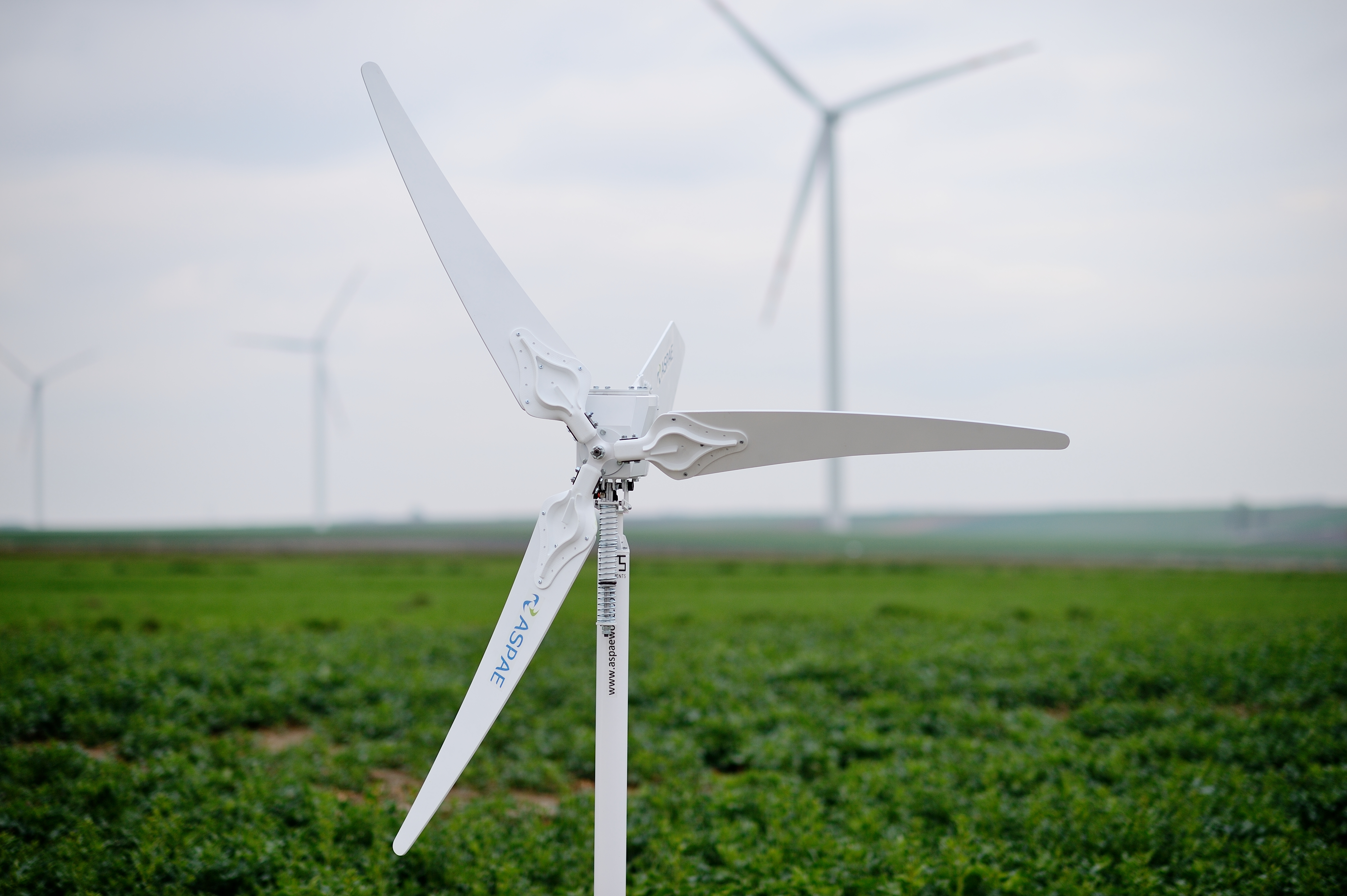 Zdjęcie przedstawia turbiny wiatrowe. Z tyłu, za turbinami widać zielone pola.