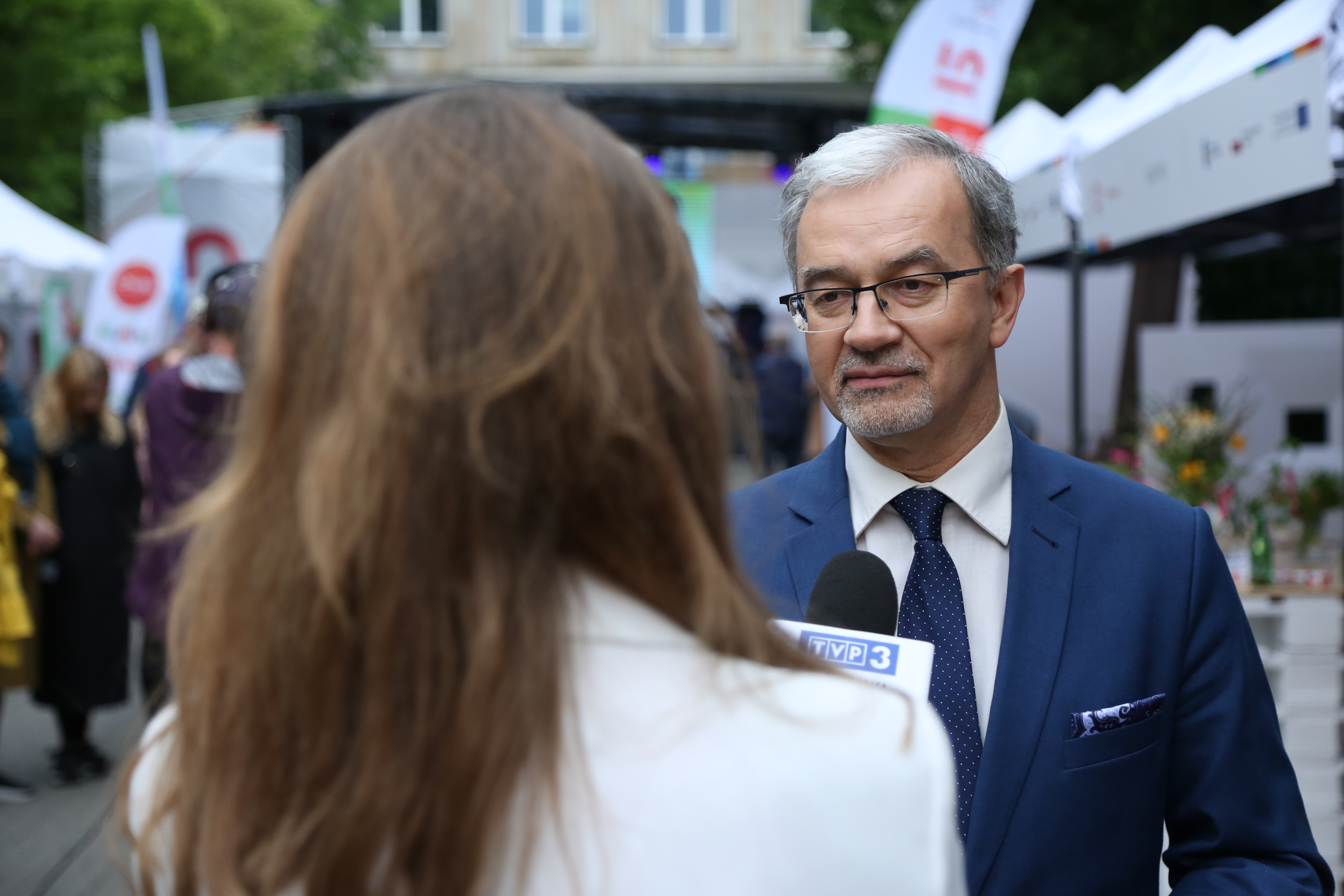Minister Jerzy Kwieciński stoi przy dziennikarce i udziela odpowiedzi do mikrofonu