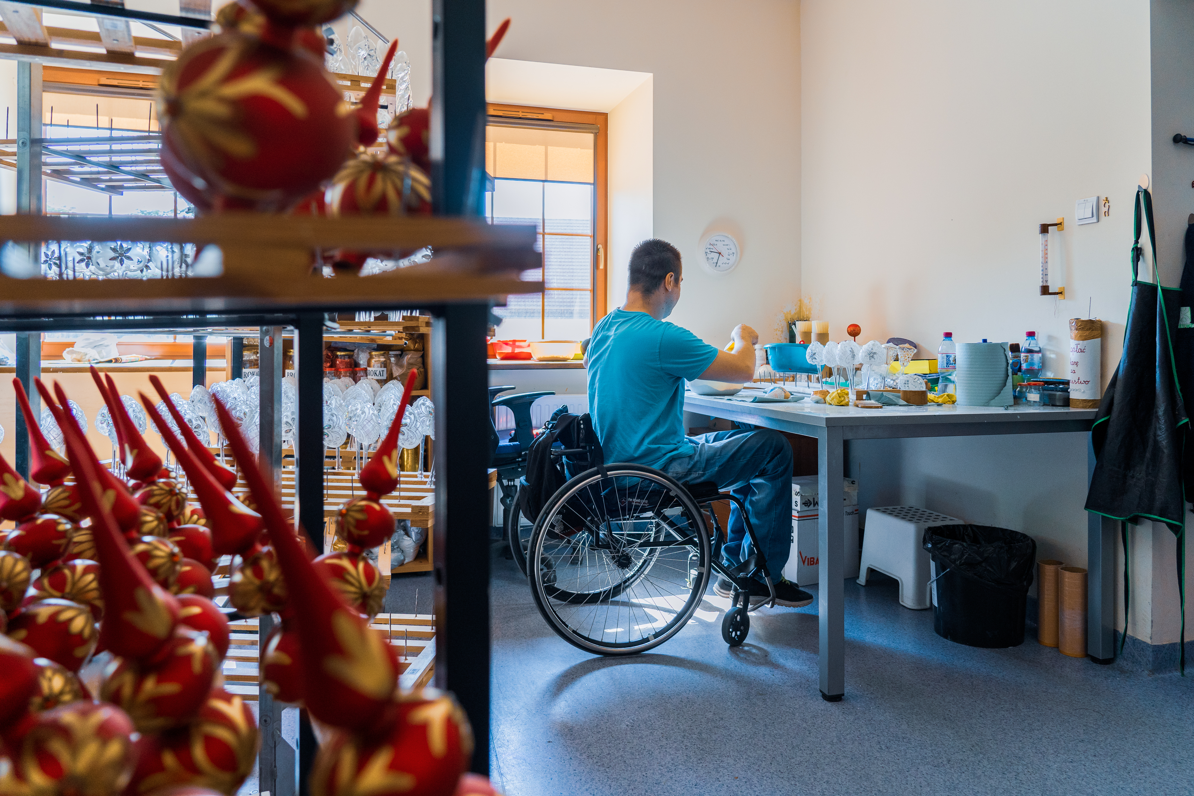 The picture shows a young, disabled man painting Christmas balls.