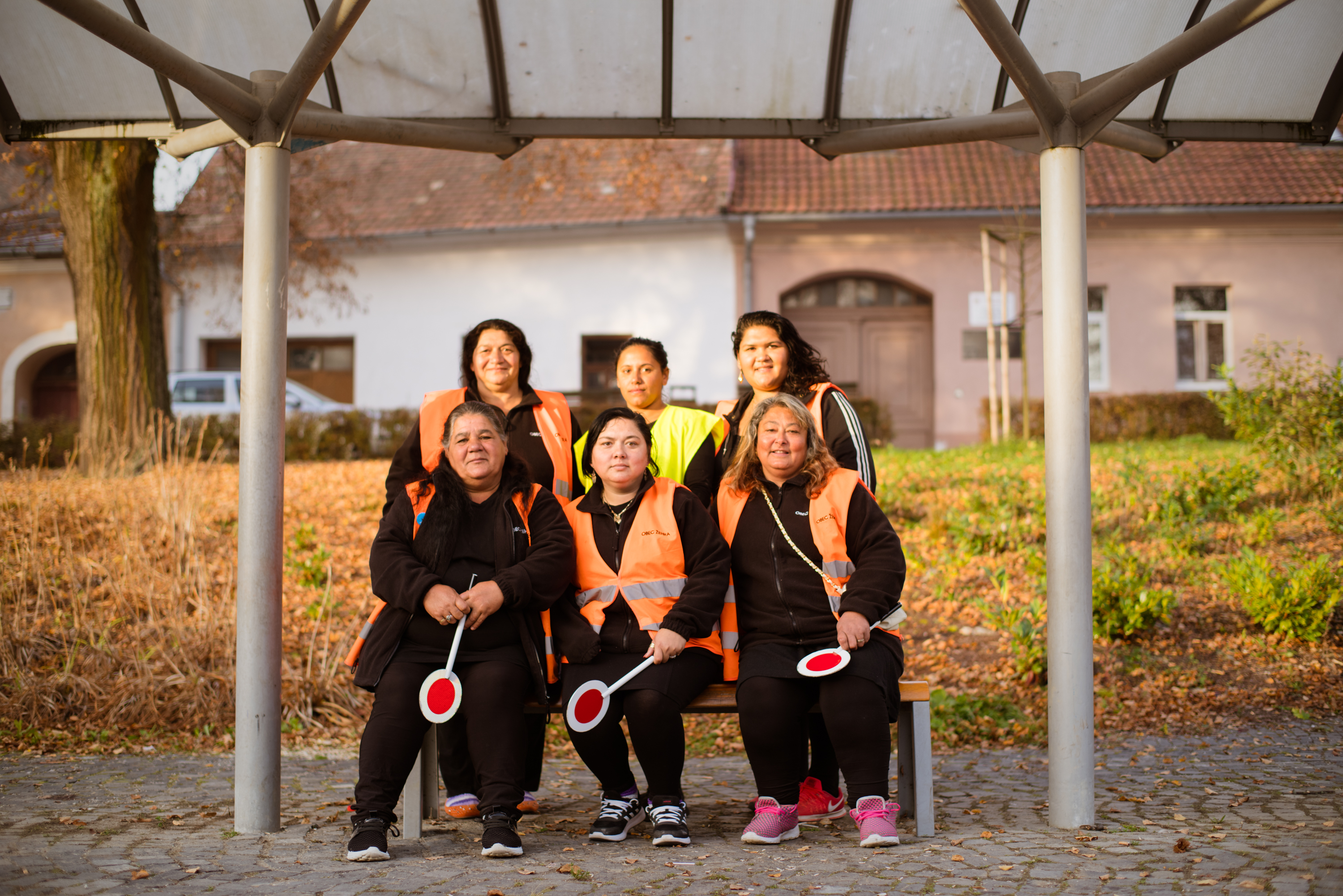 Six women with vests and handheld stop signs sitting at the bus stop. Phot. Erik Švec